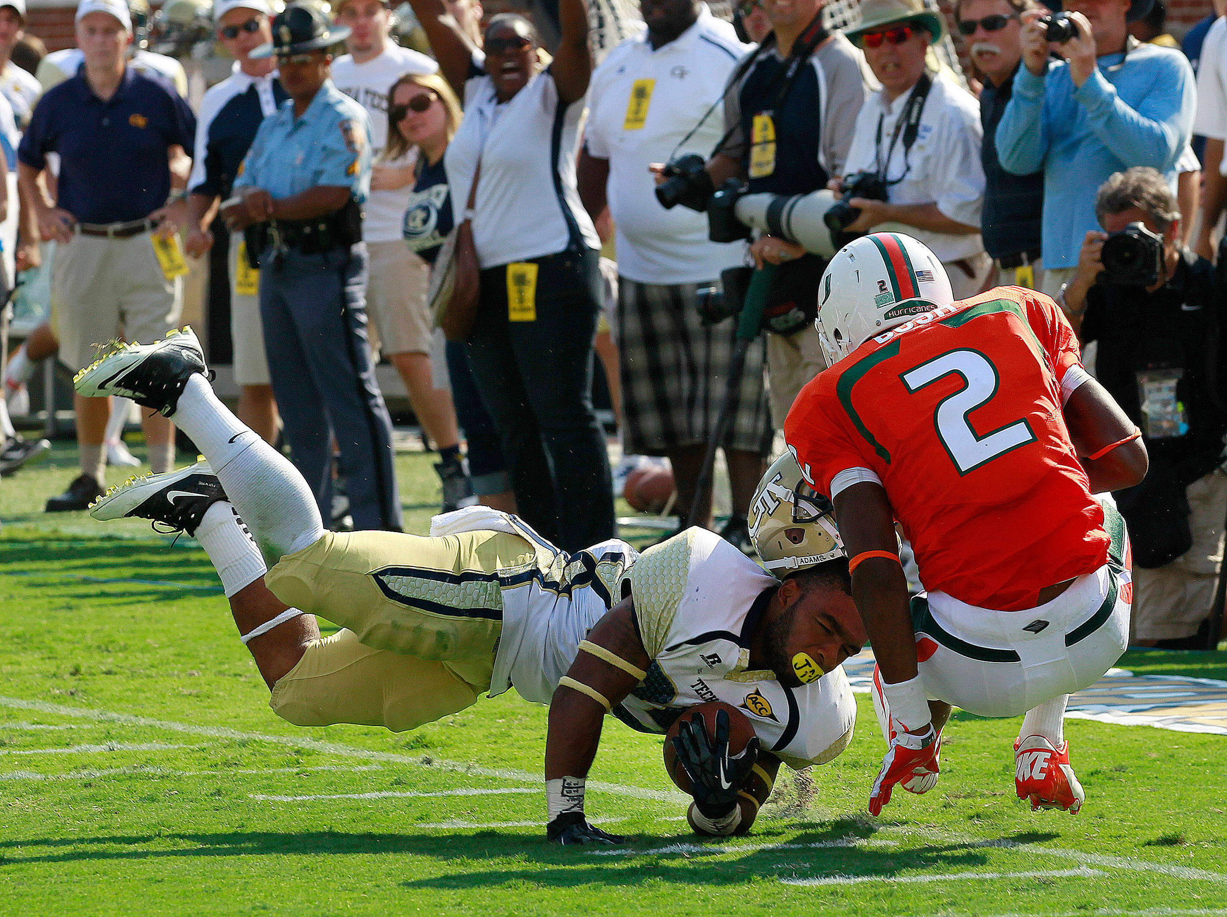 Georgia Tech running back Robert Godhigh (25) has his helmet ripped off by Miami defensive back Deon Bush (2) after a catch in the first half of an NCAA college football game in Atlanta on Saturday, Sept. 22, 2012. Bush was charged with a facemask penalty on the play. (AP Photo/John Bazemore)